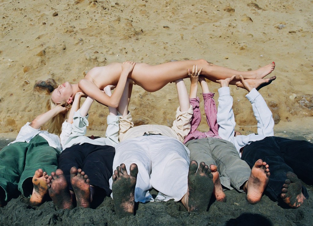 Group of people holding up a woman on a sandy beach. The focus is on the group's collective effort in a sunny, outdoor setting.
