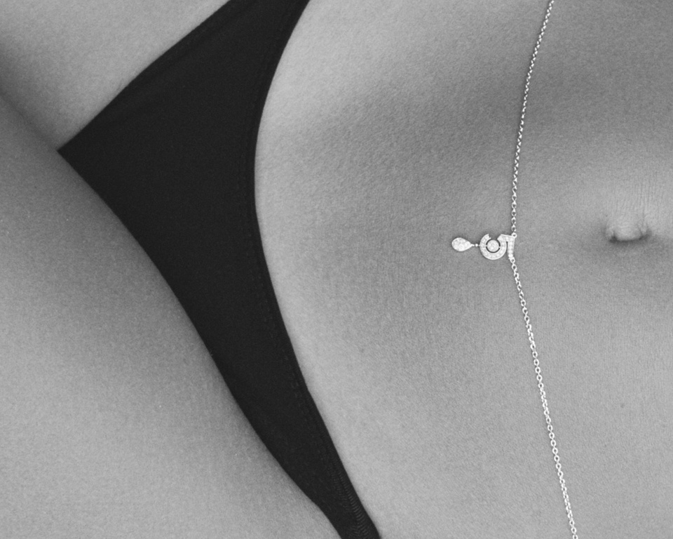 Close-up shot of a slender adult female torso adorned with a silver belly chain and black bikini bottom. Black and white photography.