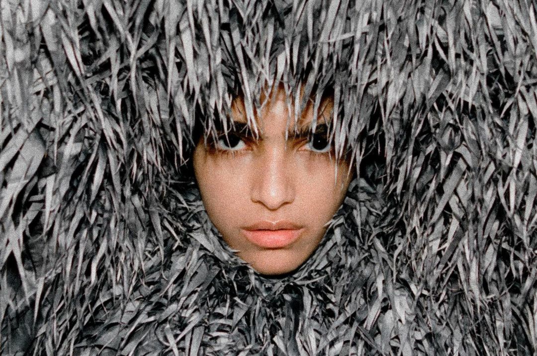 Close-up portrait of a model's face framed entirely by dense, textured grey fringed apparel shot by Thistle Brown.