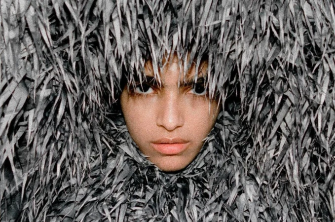Close-up portrait of a model's face framed entirely by dense, textured grey fringed apparel shot by Thistle Brown.