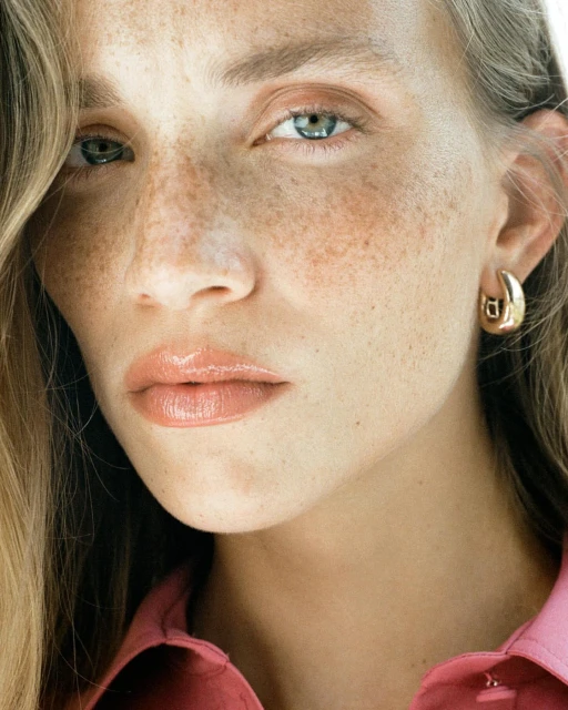 Close-up portrait of a fair-skinned adult female with freckles, wearing a pink top and gold hoop earrings, showcasing beauty.