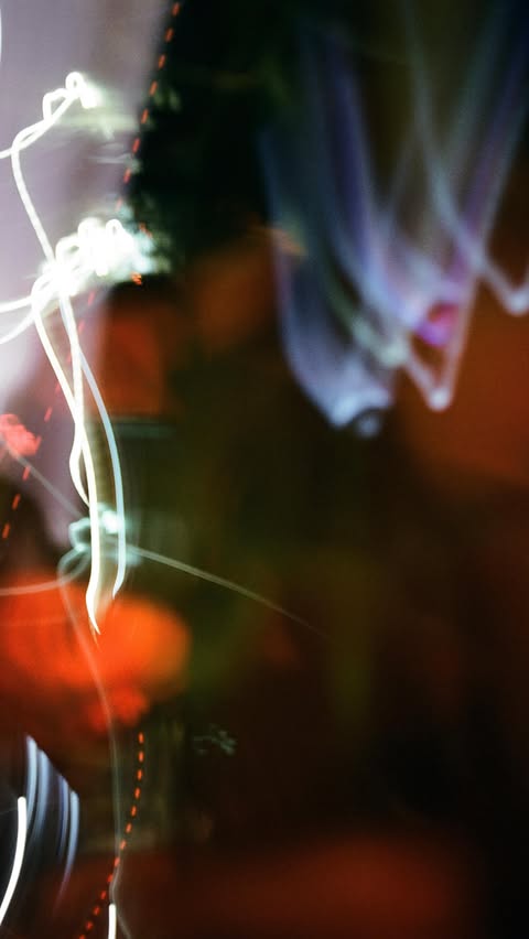 Abstract composition with blurred light trails in shades of white, purple, and orange against a dark background.