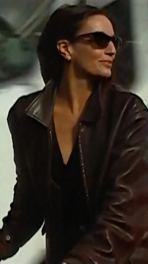 Woman wearing dark sunglasses and a dark leather jacket looking aside outdoors
