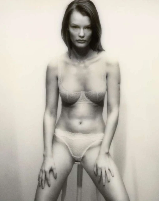 Artistic studio portrait of a woman in lingerie, posing with hands on a stool, soft lighting, and neutral tones.