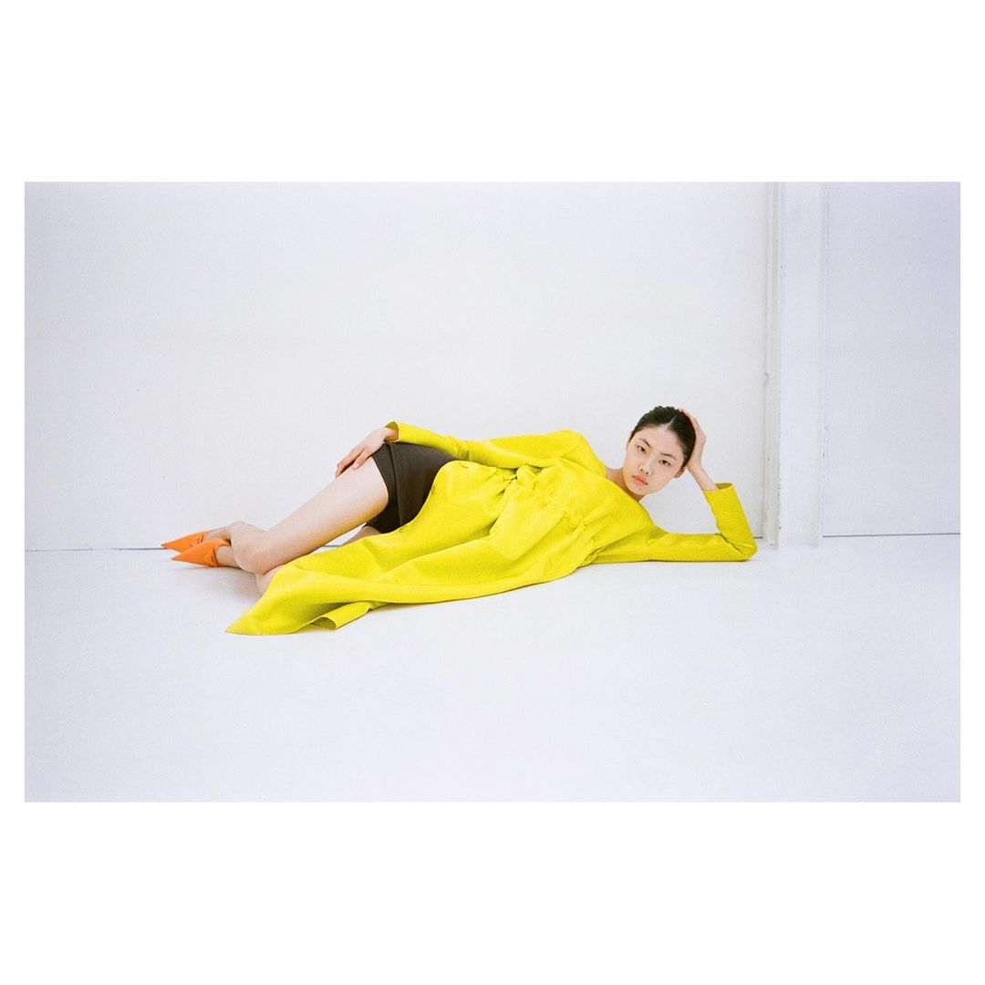 Model wearing a vibrant yellow coat lying on a white studio floor shot by Thistle Brown