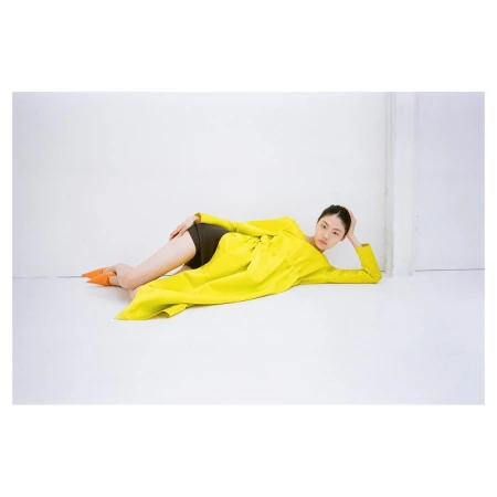 Model wearing a vibrant yellow coat lying on a white studio floor shot by Thistle Brown