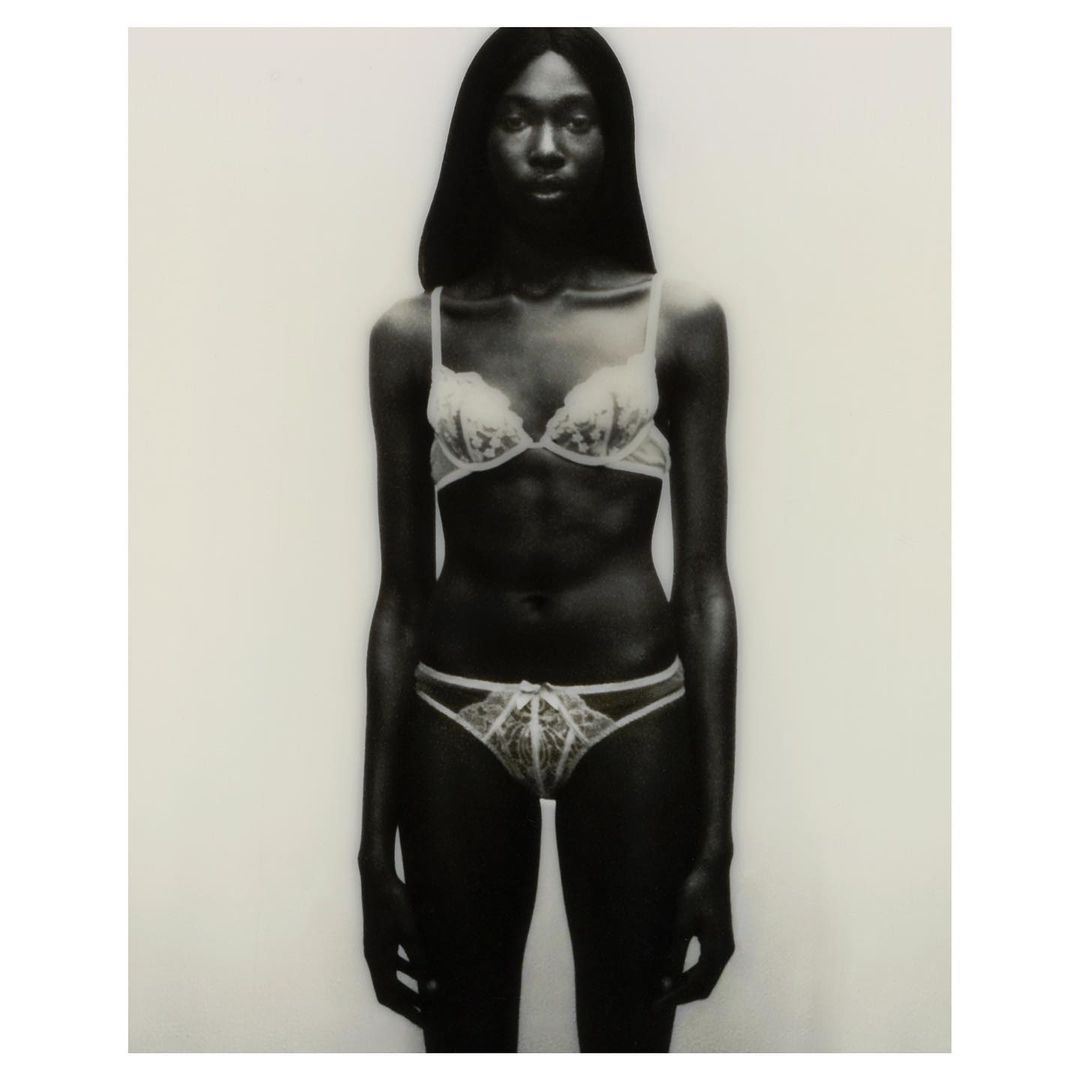 Studio shot of an adult female in a bra and underwear standing against a white background. The image is desaturated with a slight vignette.