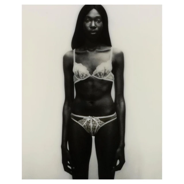 Studio shot of an adult female in a bra and underwear standing against a white background. The image is desaturated with a slight vignette.