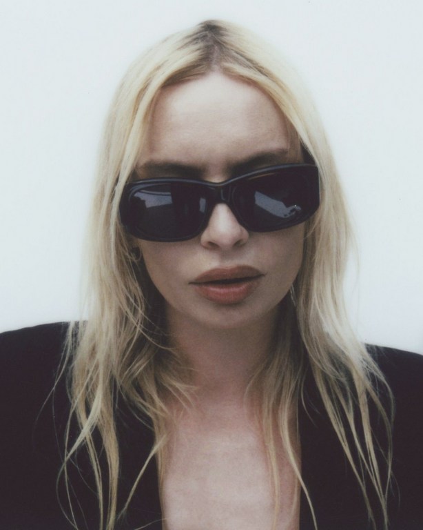 Close-up portrait of a woman with blonde hair wearing dark sunglasses against a plain white background.