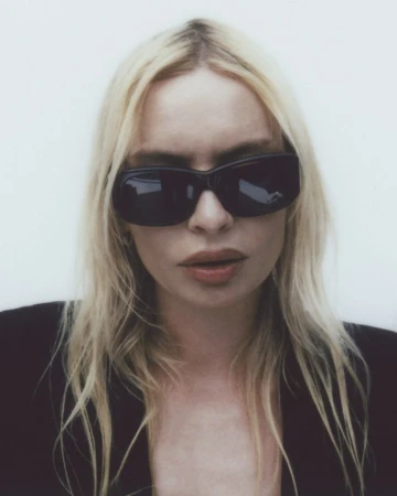 Close-up portrait of a woman with blonde hair wearing dark sunglasses against a plain white background.