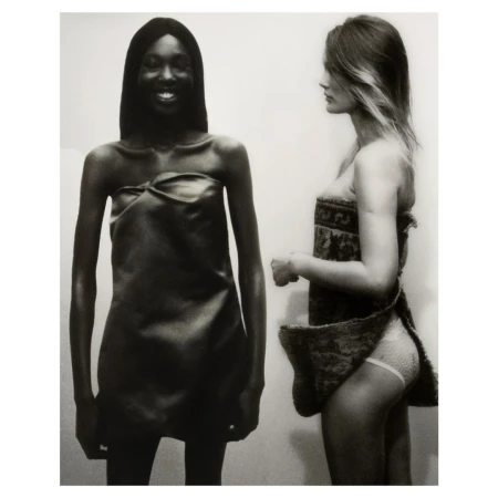 Monochrome shot of two fashion models in dresses, one with dark skin smiling, the other with light skin in profile, against a plain background.