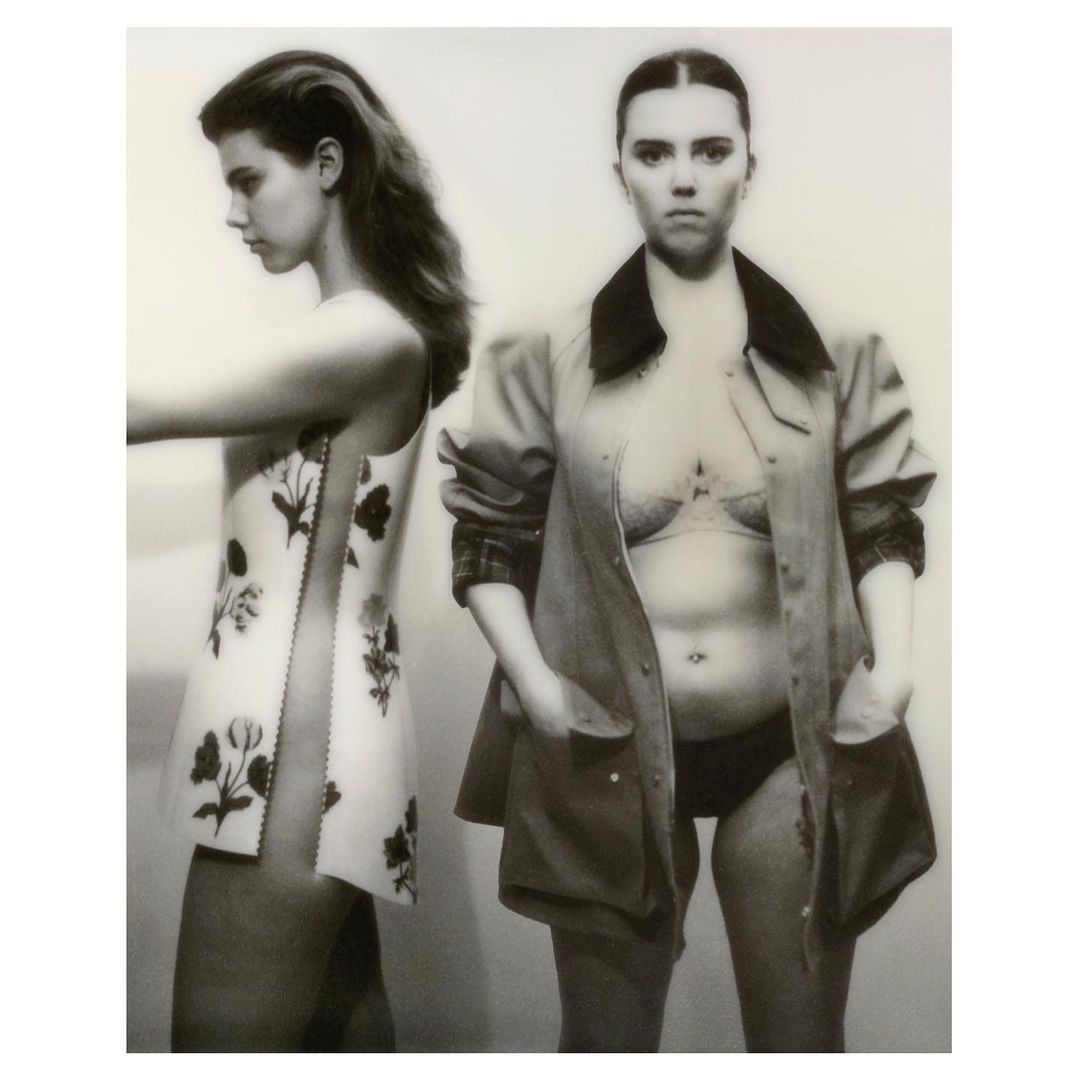 Black and white fashion shot of two fair-skinned women. One woman wears floral dress and the other is in a jacket with lingerie.