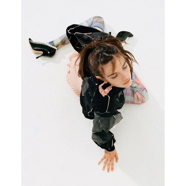Overhead shot of a stylish woman posing in a black jacket, printed leggings, and high heels on a clean white backdrop.