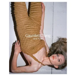 Model wearing textured amber smocked jumpsuit lying upside down on pale surface