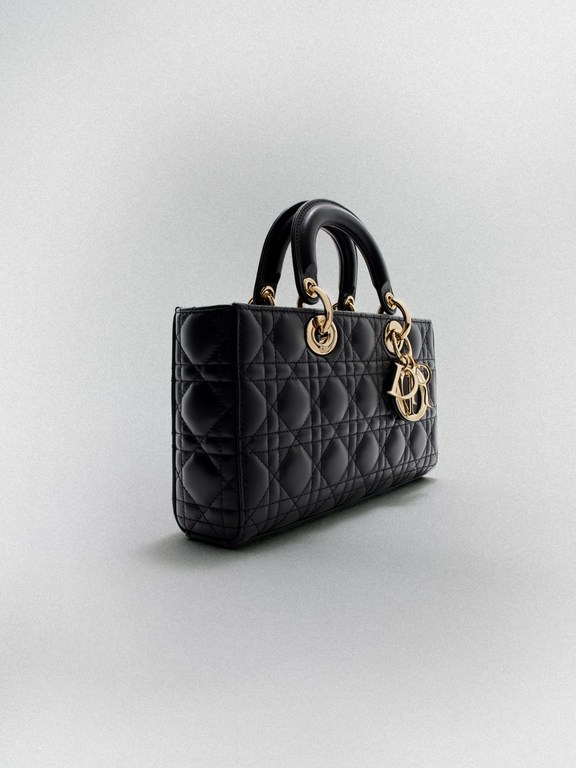 Elegant black leather Lady Dior handbag with gold hardware and signature charm, displayed against a soft grey studio backdrop.