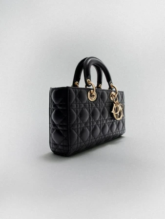 Elegant black leather Lady Dior handbag with gold hardware and signature charm, displayed against a soft grey studio backdrop.