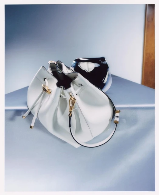 Elegant white leather bucket bag on a light blue surface with a black and white patterned vase in a minimalist fashion photography style.