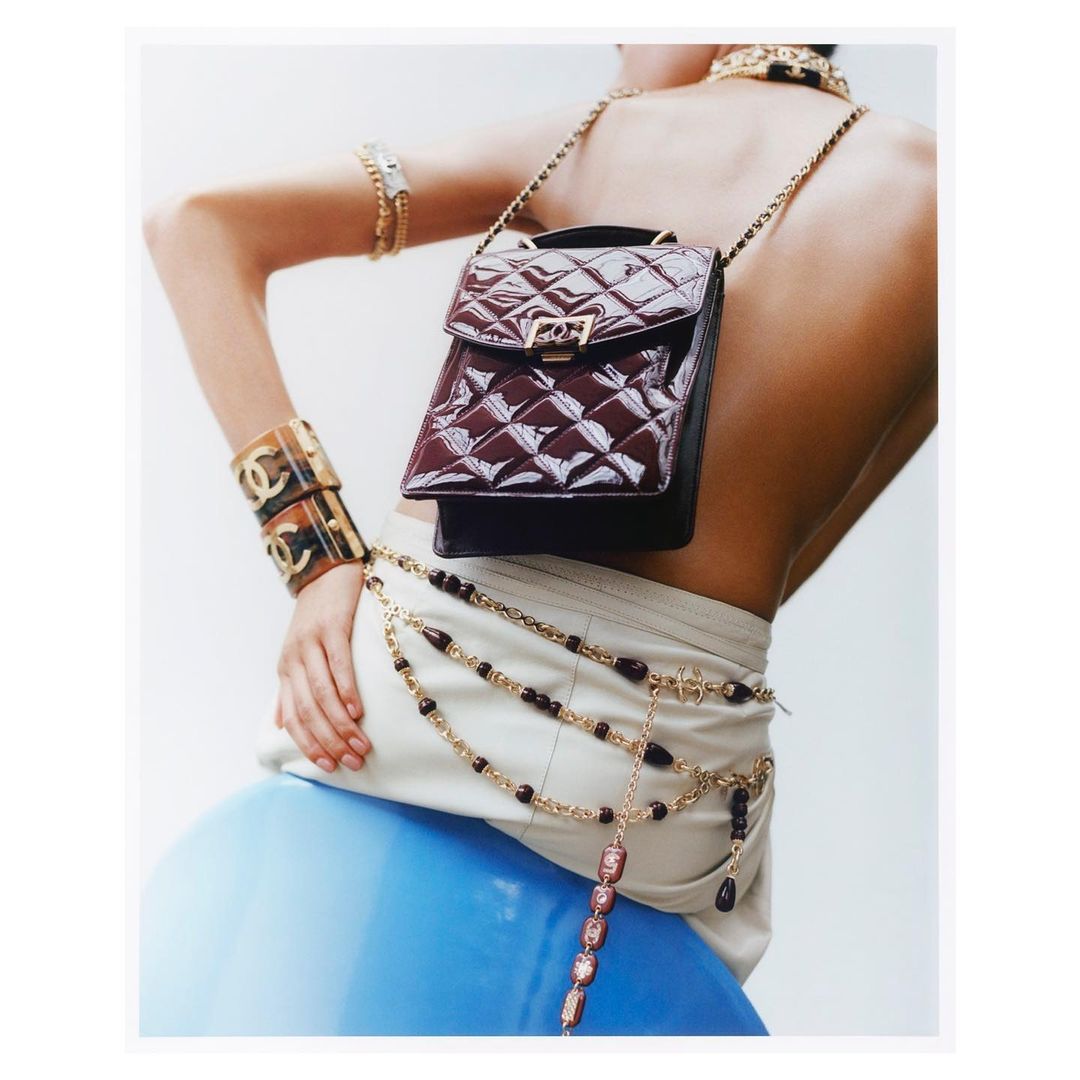 Fashion shot features a model wearing jewelry and a handbag with a blue ball in the background in a studio environment.