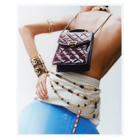 Fashion shot features a model wearing jewelry and a handbag with a blue ball in the background in a studio environment.