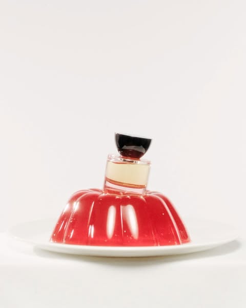 Still life shot of red gelatin dessert on a white plate, topped with two small glass containers in a bright, minimalist setting.
