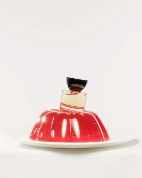 Still life shot of red gelatin dessert on a white plate, topped with two small glass containers in a bright, minimalist setting.
