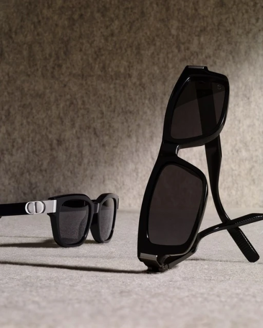 Two pairs of black frame sunglasses are arranged on a surface against a textured grey backdrop, displaying eyewear fashion.