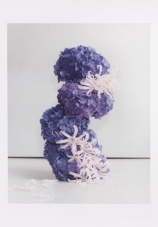 Tower of blue and purple hydrangeas arranged with decorative ribbons in a studio setting, creating a visually striking floral composition.
