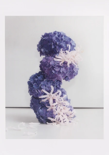Tower of blue and purple hydrangeas arranged with decorative ribbons in a studio setting, creating a visually striking floral composition.