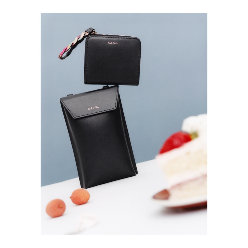 Black Paul Smith wallet and card holder float against a blue background with a partial view of a strawberry shortcake and two lychees.