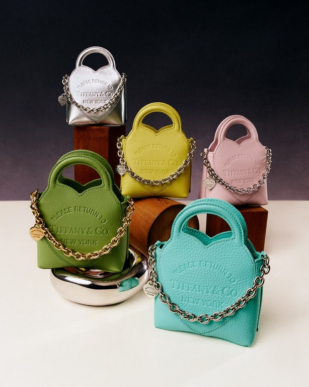 Colorful miniature Tiffany & Co. heart-shaped handbags with chain straps, arranged on a wooden and white surface in studio lighting.