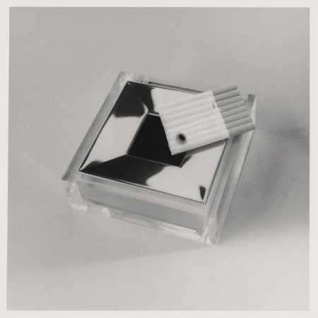 Close-up studio shot of a clear ashtray with a silver inset, accompanied by cigarettes in a plastic case, all on a neutral background.