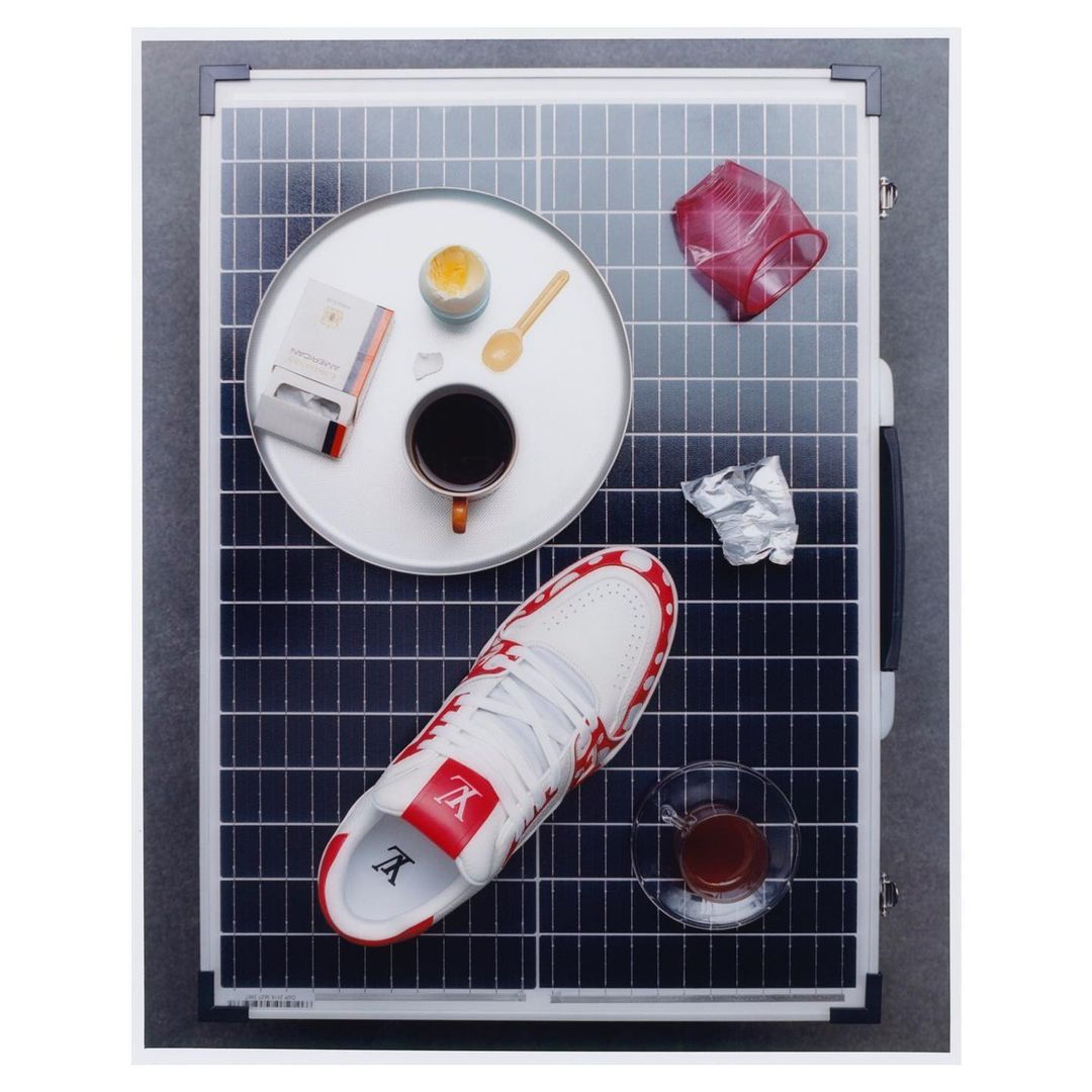 Overhead shot of a solar panel with a sneaker, coffee, cigarette pack, and other objects arranged on it, in a studio setting.