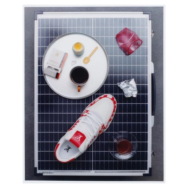 Overhead shot of a solar panel with a sneaker, coffee, cigarette pack, and other objects arranged on it, in a studio setting.