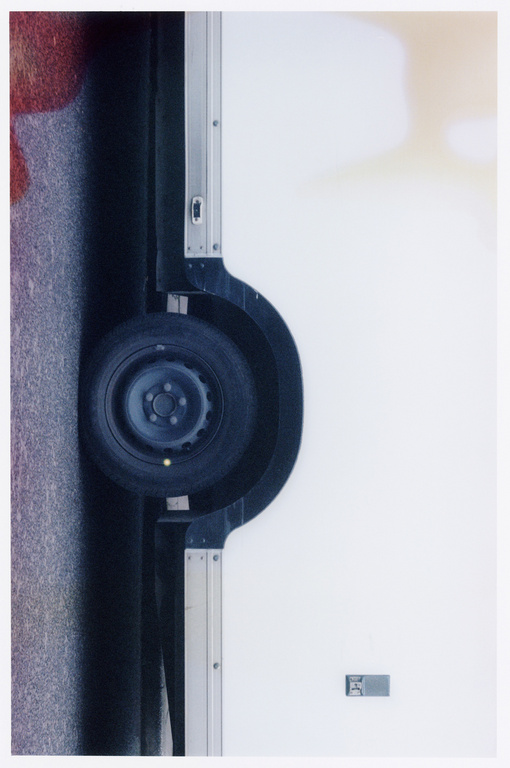 Automotive scene featuring a tire mounted on a white truck body, set against a gray road, showcasing details of vehicle design.