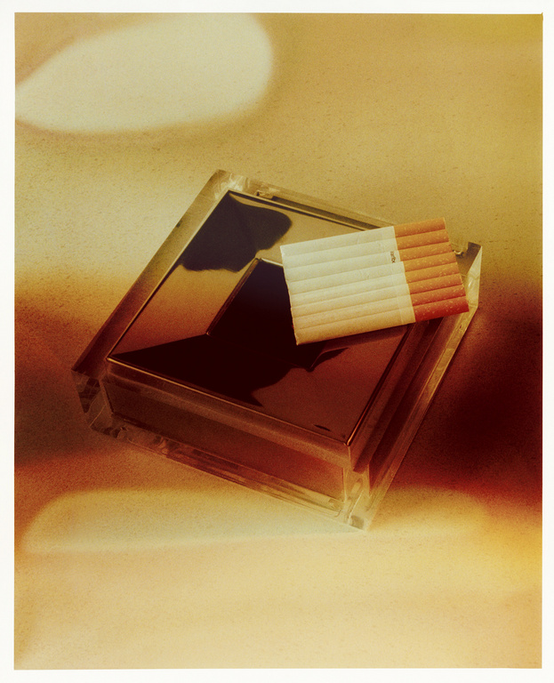 Pack of cigarettes rests on a mirrored container in a vintage-style, close-up studio shot with diffused lighting, creating a retro aesthetic.