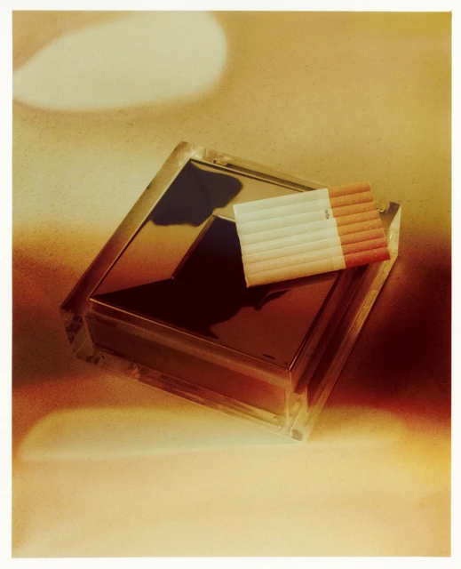 Pack of cigarettes rests on a mirrored container in a vintage-style, close-up studio shot with diffused lighting, creating a retro aesthetic.