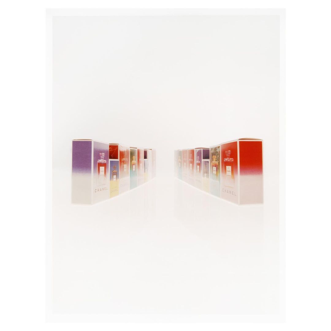 A series of Chanel perfume boxes are displayed on a white surface, arranged in two parallel rows with various colors and sizes.