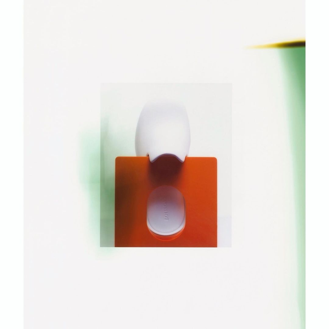 A white plastic device sits on an orange stand against a bright background, with studio lighting highlighting its sleek design.