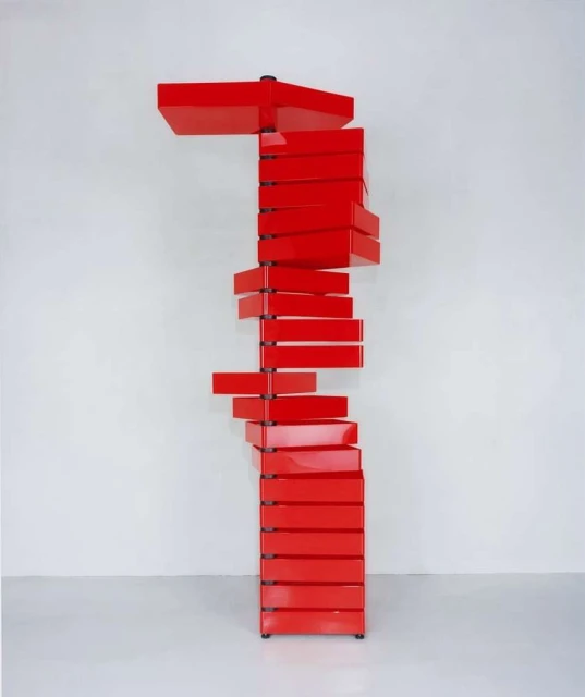 Unique red shelf, chest of drawers with a spiral design, stands in front of a white wall and floor. Perfect for home or design studio.