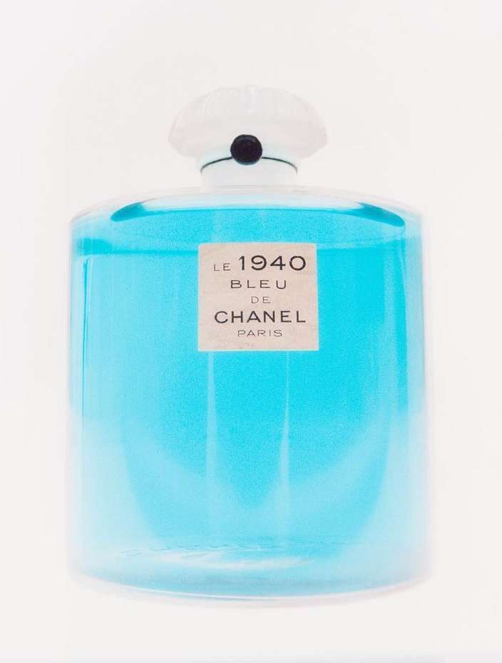 A clear glass perfume bottle filled with bright blue liquid against a seamless white background.