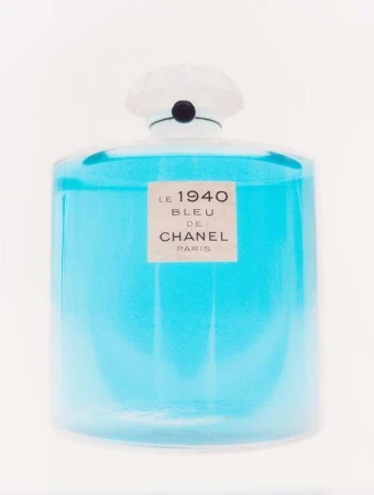 A clear glass perfume bottle filled with bright blue liquid against a seamless white background.