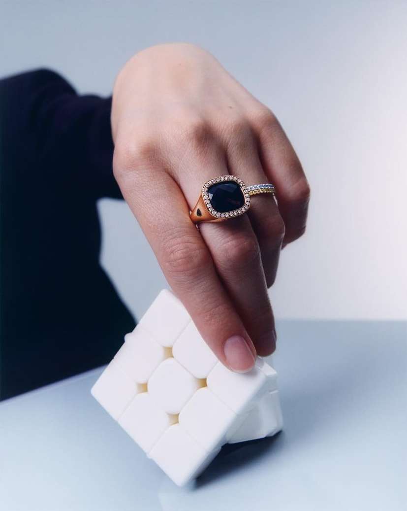 Close-up of a hand holding a Rubik's cube near gold rings, capturing a blend of fashion and puzzle-solving elements in a studio setting.