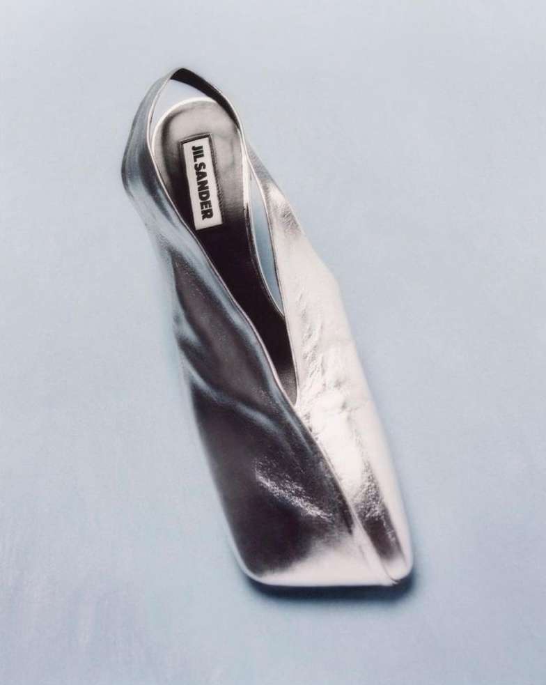 Elevated view of a metallic silver Jil Sander shoe on a light blue background, highlighting its sleek design and reflective surface.