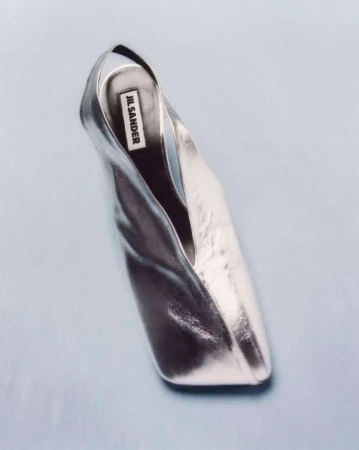Elevated view of a metallic silver Jil Sander shoe on a light blue background, highlighting its sleek design and reflective surface.