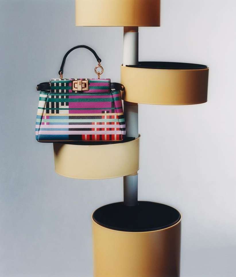 Colorful striped handbag displayed on a modern display stand with cylindrical tiers against a neutral background in a studio setting.