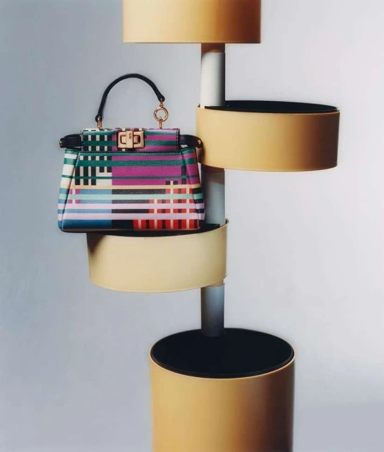 Colorful striped handbag displayed on a modern display stand with cylindrical tiers against a neutral background in a studio setting.