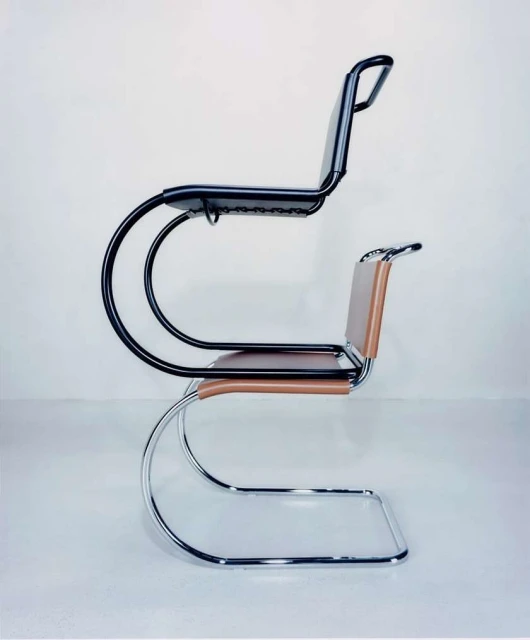Side view of two cantilever chairs, one black and one tan leather, stacked on top of each other against a light grey backdrop.