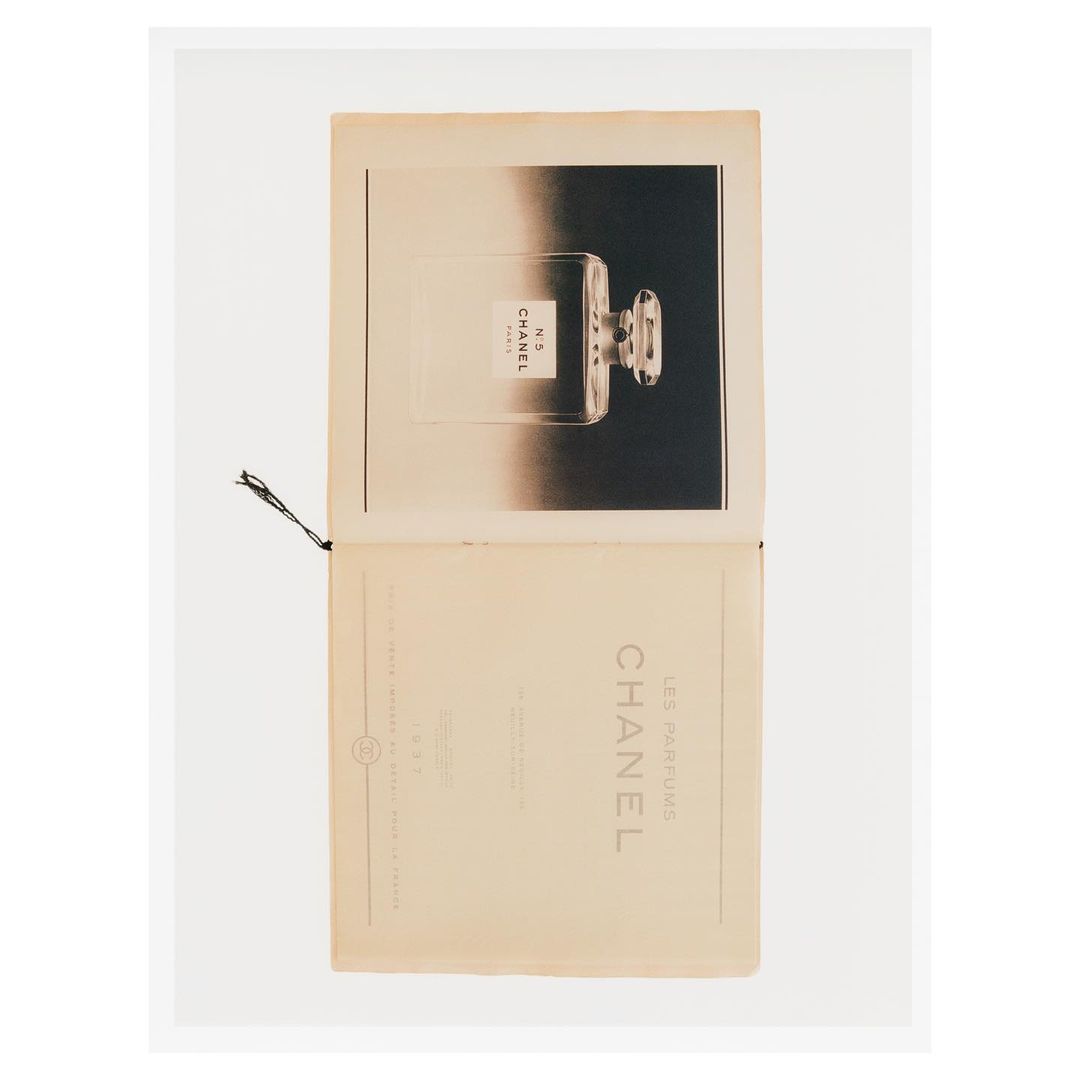 Chanel No. 5 perfume advertisement in a magazine. The perfume bottle is on a dark background with light text on the bottom page.