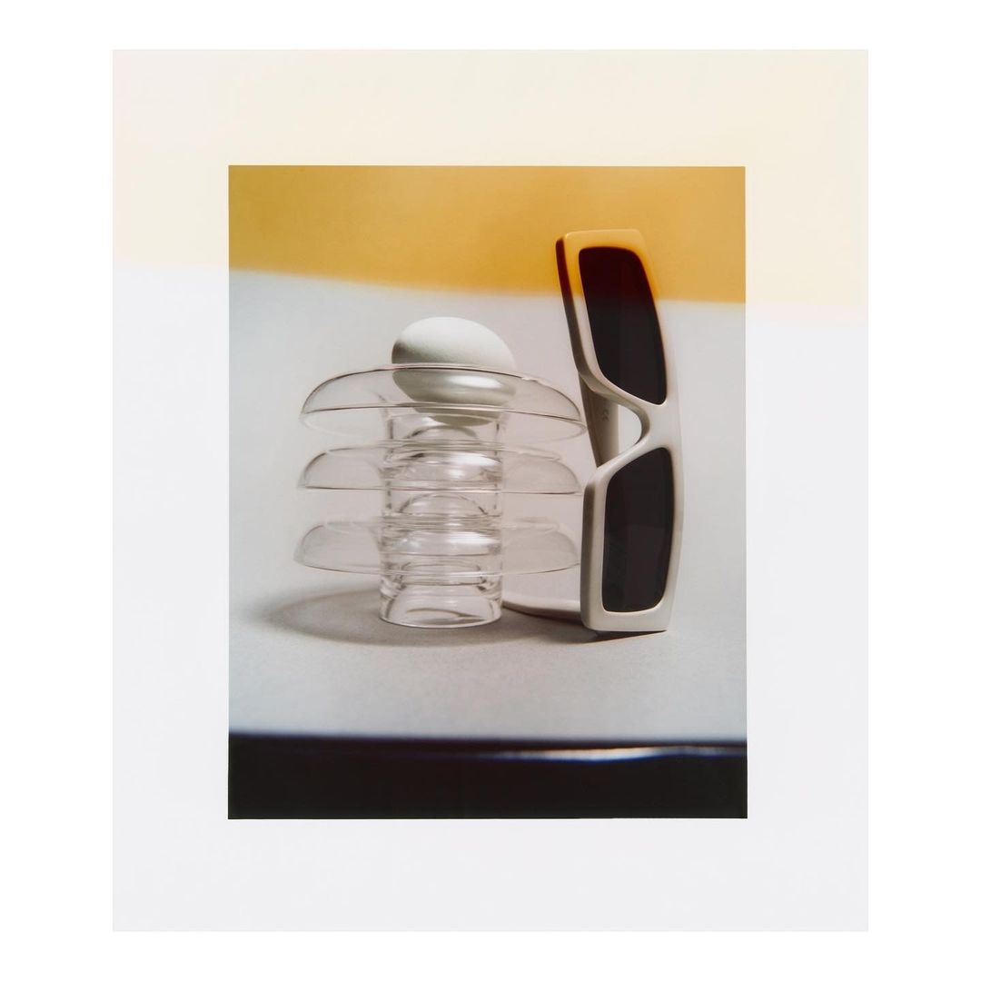 Modern still life featuring sunglasses and an egg on a glass stand against a gradient background, capturing a minimalist aesthetic.