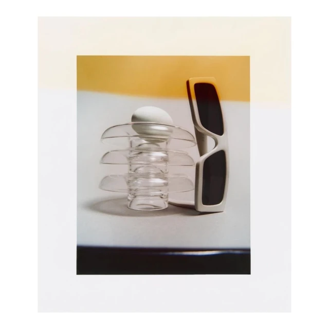 Modern still life featuring sunglasses and an egg on a glass stand against a gradient background, capturing a minimalist aesthetic.